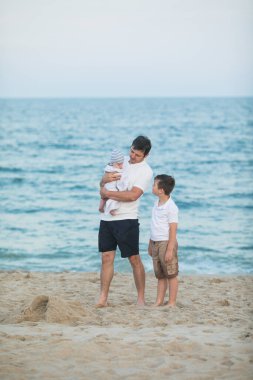 Baba ve çocuk gün batımında tropik plajda oynuyorlar. Deniz tatil beldesinde aile tatili. Babam güneşli bir akşamda çocuklarla okyanus kıyısında oynuyor. Çocuklarla seyahat et. Ebeveyn sevgisi