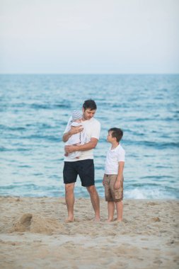 Baba ve çocuk gün batımında tropik plajda oynuyorlar. Deniz tatil beldesinde aile tatili. Babam güneşli bir akşamda çocuklarla okyanus kıyısında oynuyor. Çocuklarla seyahat et. Ebeveyn sevgisi