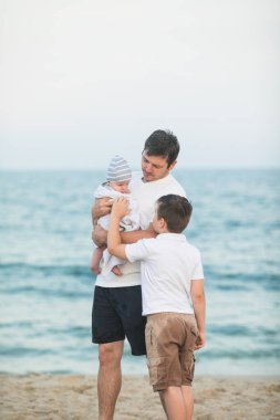 Baba ve çocuk gün batımında tropik plajda oynuyorlar. Deniz tatil beldesinde aile tatili. Babam güneşli bir akşamda çocuklarla okyanus kıyısında oynuyor. Çocuklarla seyahat et. Ebeveyn sevgisi