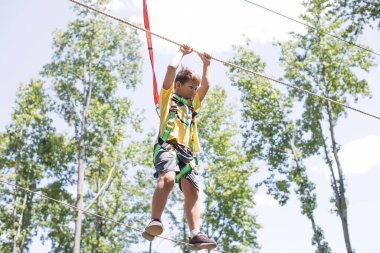 Okullu çocuk zeplin macerasına hazırlanıyor. Dağlara tırmanmak yaz eğlencesidir. Sıcak ve güneşli bir yaz gününde macera parkına tırmanmanın tadını çıkarıyorum. Küçük çocuklar için yaz etkinlikleri. 