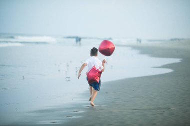 Mutlu çocuk plajda kırmızı balonlarla oynar ve yaz tatillerinde harika vakit geçirir. Yaşam tarzı, tatil, mutluluk, eğlence konsepti
