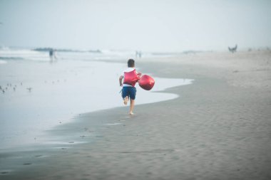 Mutlu çocuk plajda kırmızı balonlarla oynar ve yaz tatillerinde harika vakit geçirir. Yaşam tarzı, tatil, mutluluk, eğlence konsepti