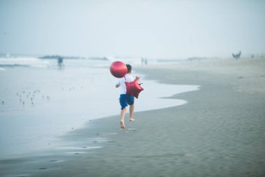 Mutlu çocuk plajda kırmızı balonlarla oynar ve yaz tatillerinde harika vakit geçirir. Yaşam tarzı, tatil, mutluluk, eğlence konsepti