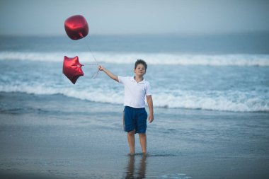 Mutlu çocuk plajda kırmızı balonlarla oynar ve yaz tatillerinde harika vakit geçirir. Yaşam tarzı, tatil, mutluluk, eğlence konsepti