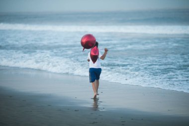 Mutlu çocuk plajda kırmızı balonlarla oynar ve yaz tatillerinde harika vakit geçirir. Yaşam tarzı, tatil, mutluluk, eğlence konsepti