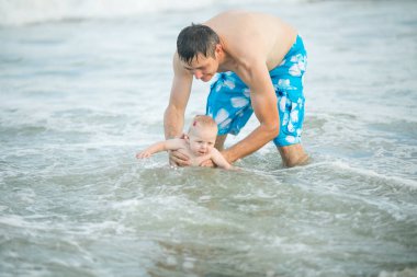Baba ve bebek okyanusta yüzüyor. Baba ve çocuk birlikte gün batımının tadını çıkarıyorlar. Sevgi dolu bekar baba, sevimli küçük oğluna sarılıyor..