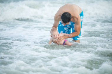 Baba ve bebek okyanusta yüzüyor. Baba ve çocuk birlikte gün batımının tadını çıkarıyorlar. Sevgi dolu bekar baba, sevimli küçük oğluna sarılıyor..