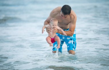 Baba ve bebek okyanusta yüzüyor. Baba ve çocuk birlikte gün batımının tadını çıkarıyorlar. Sevgi dolu bekar baba, sevimli küçük oğluna sarılıyor..
