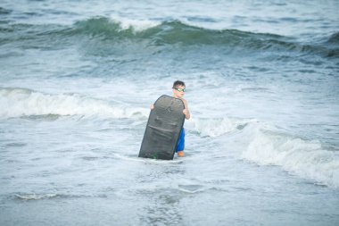 Küçük sörfçü deniz dalgasında sörf yapmayı öğreniyor. Çocuk yaz okyanusunda oynuyor, sörf öğreniyor, dalgalara biniyor. Küçük çocuk sörf tahtasında yüzüyor.