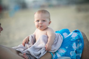 Baba, güzel oğlunu gün batımında kumsalda tutuyor. Okyanus sahilinde mutlu bir bebek.