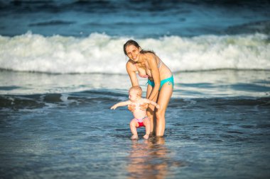 Anne, okyanus dalgasında bebeğine sarılıyor. Genç bir anne ve güzel çocuğu arasındaki bağ ve birliktelik kavramı..