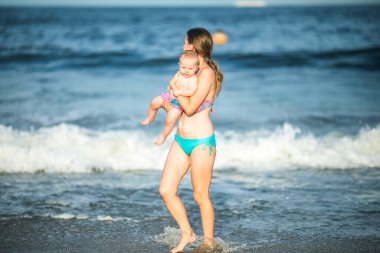 Anne, okyanus dalgasında bebeğine sarılıyor. Genç bir anne ve güzel çocuğu arasındaki bağ ve birliktelik kavramı..