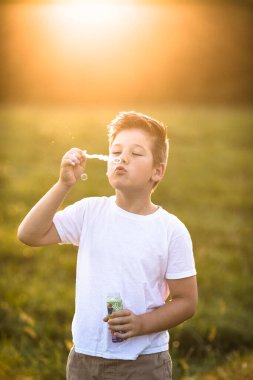 Şirin küçük çocuk dışarıda büyük sabun köpükleriyle oynuyor. Çocuk aynı anda hem büyük hem de küçük kabarcıklar çıkarıyor. Çocuklar için aktif yaz tatili.