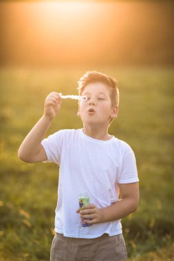 Şirin küçük çocuk dışarıda büyük sabun köpükleriyle oynuyor. Çocuk aynı anda hem büyük hem de küçük kabarcıklar çıkarıyor. Çocuklar için aktif yaz tatili.