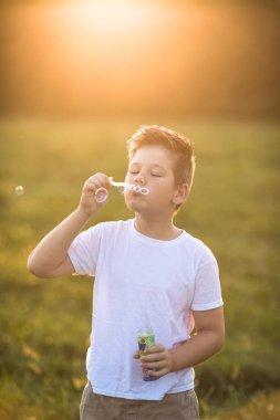 Şirin küçük çocuk dışarıda büyük sabun köpükleriyle oynuyor. Çocuk aynı anda hem büyük hem de küçük kabarcıklar çıkarıyor. Çocuklar için aktif yaz tatili.