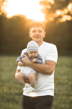 Mutlu aile kucaklaşmaları ve yaz yürüyüşlerinde kucaklaşmaları. Baba ve iki oğlu parkta yürüyor ve güzel doğanın tadını çıkarıyorlar. Sevimli bir aile fotoğrafı..