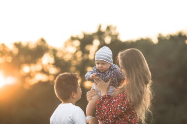 Güneşli bir günde doğanın tadını çıkaran mutlu bir anne ve oğlu. Güzel, genç bir annenin sevimli oğluna sarılıp oyun oynaması.
