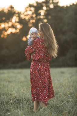Güneşli bir günde doğanın tadını çıkaran mutlu bir anne ve oğlu. Güzel, genç bir annenin sevimli oğluna sarılıp oyun oynaması.