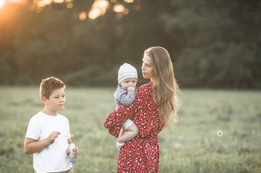 Güneşli bir günde doğanın tadını çıkaran mutlu bir anne ve oğlu. Güzel, genç bir annenin sevimli oğluna sarılıp oyun oynaması.