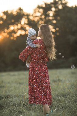 Güneşli bir günde doğanın tadını çıkaran mutlu bir anne ve oğlu. Güzel, genç bir annenin sevimli oğluna sarılıp oyun oynaması.