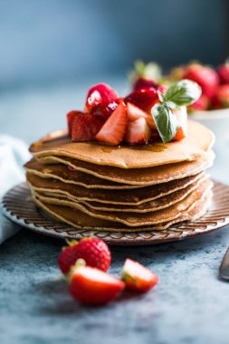 Beyaz tabakta servis edilen taze yaban mersinli, ahududulu ve ballı Amerikan gözlemeleri. Krep ve sütle sağlıklı bir sabah kahvaltısı.