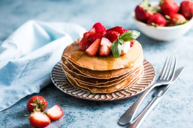 Beyaz tabakta servis edilen taze yaban mersinli, ahududulu ve ballı Amerikan gözlemeleri. Krep ve sütle sağlıklı bir sabah kahvaltısı.