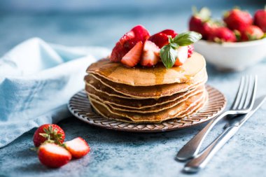 Beyaz tabakta servis edilen taze yaban mersinli, ahududulu ve ballı Amerikan gözlemeleri. Krep ve sütle sağlıklı bir sabah kahvaltısı.
