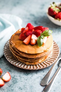 Beyaz tabakta servis edilen taze yaban mersinli, ahududulu ve ballı Amerikan gözlemeleri. Krep ve sütle sağlıklı bir sabah kahvaltısı.