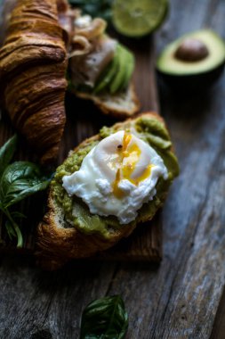 Jamon jambonlu kruvasan sandviçler serrano paleta iberica, avokado, fesleğen, mavi arka planda yumurta pashot. Lezzetli aperatifler, mezeler, tapalar..