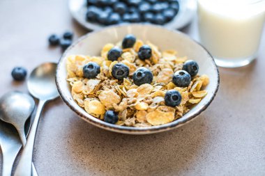 Sağlıklı bir vejetaryen yoğurt kahvaltısı kavramı, tam tahıllı mısır gevreği taze meyvesi mavi bir masada beyaz mutfak arka planına karşı. Ön görünüm.