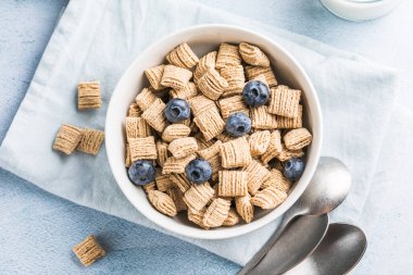 Sağlıklı bir vejetaryen yoğurt kahvaltısı kavramı, tam tahıllı mısır gevreği taze meyvesi mavi bir masada beyaz mutfak arka planına karşı. Ön görünüm.