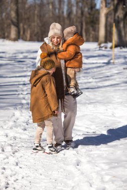 Kış hafta sonu. Anne ve iki oğlu sıcak kış kıyafetleri içinde ağaçların arasındaki ormanda eğlenirken yürüyorlar.
