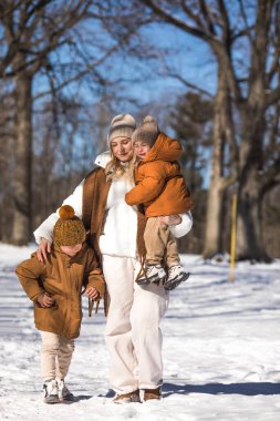 Kış hafta sonu. Anne ve iki oğlu sıcak kış kıyafetleri içinde ağaçların arasındaki ormanda eğlenirken yürüyorlar.