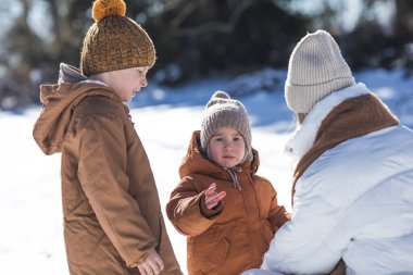 Kış hafta sonu. Anne ve iki oğlu sıcak kış kıyafetleri içinde ağaçların arasındaki ormanda eğlenirken yürüyorlar.