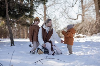 Aktif ve mutlu bir anne, küçük oğullarıyla birlikte kış ormanlarında bir yol boyunca yürür. Kış aile tatili. Mutlu annelik.