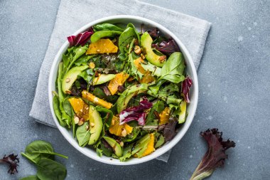 Taze salata organik avokado ve beyaz tabakta portakal ve zeytinyağlı ıspanak yaprakları. vejetaryen yemeği.