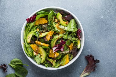 Taze salata organik avokado ve beyaz tabakta portakal ve zeytinyağlı ıspanak yaprakları. vejetaryen yemeği.