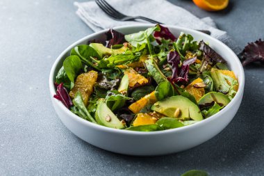 Taze salata organik avokado ve beyaz tabakta portakal ve zeytinyağlı ıspanak yaprakları. vejetaryen yemeği.
