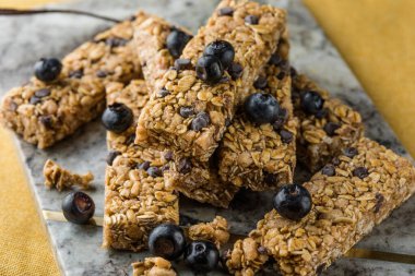 Arka planda çeşitli granola barlar var. Mısır gevreği gofretleri. Yulaf, fındık ve böğürtlenli kahvaltılık barlar..