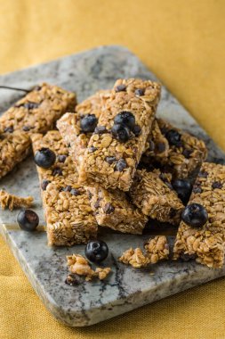 Arka planda çeşitli granola barlar var. Mısır gevreği gofretleri. Yulaf, fındık ve böğürtlenli kahvaltılık barlar..