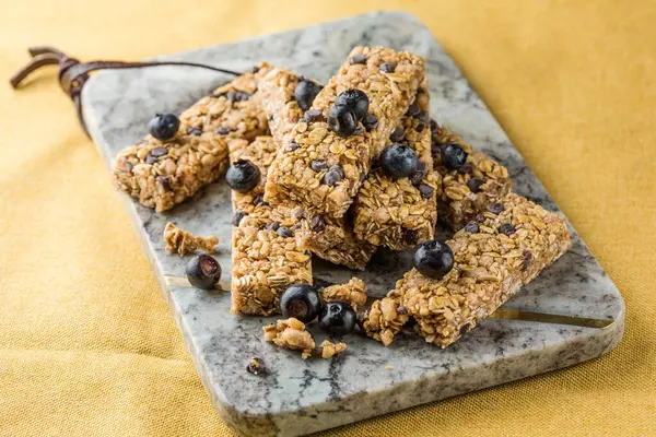 Arka planda çeşitli granola barlar var. Mısır gevreği gofretleri. Yulaf, fındık ve böğürtlenli kahvaltılık barlar..