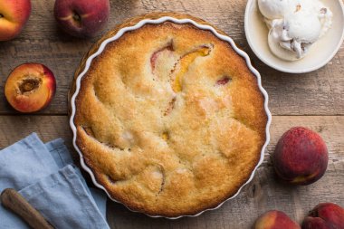 Mutfaktaki ahşap masada ev yapımı şeftali turtası yemek kitabı, toz şeker ve şeftali.
