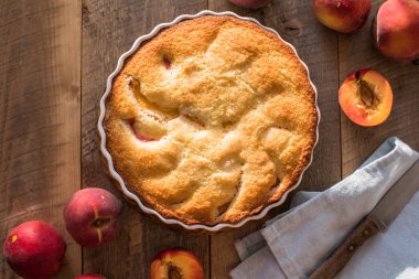 Mutfaktaki ahşap masada ev yapımı şeftali turtası yemek kitabı, toz şeker ve şeftali.