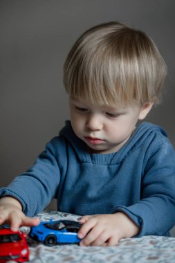 Küçük çocuk salonda bir sürü oyuncakla, arabalarla oynuyor.