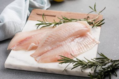 Beton arka planda bir dilim limon ve bitkiyle Tilapia filetosu.