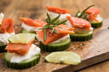 Aperatif kanepe. Krem peynirle kaplı taze salatalık dilimleri ve otlarla süslenmiş füme somon balığı.