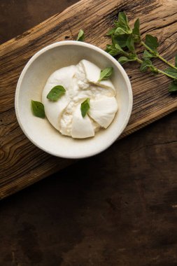 İtalyan peynirli burrata taze kekliklerle servis edilen küçük tahta kesme tahtasının üzerinde.