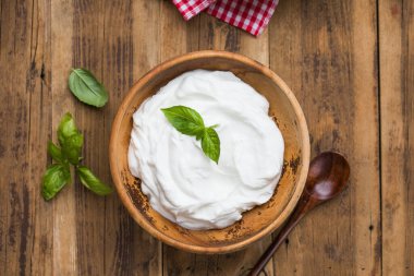 Koyu ve kremalı Yunan yoğurdu, ahşap bir kasede servis ediliyor. Sağlıklı süt ürünleri, kahvaltı, aperatif ya da temiz yeme tarzı için mükemmel.