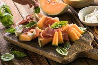 Taze İtalyan aperatifleri jamon iberico ile kavun dilimleri, kremalı burrata peyniri ve fesleğen yaprakları, ahşap bir tahtada çok güzel servis ediliyor. Gurme yemekler, Akdeniz mutfağı, sağlıklı yiyecekler.