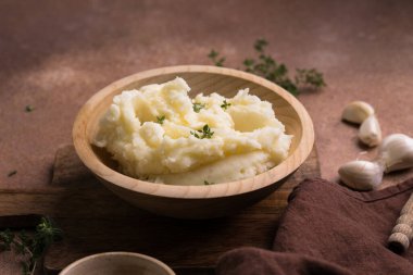 Tahta masadaki ahşap bir kasede servis edilen taze kekik ile kremalı patates püresi..